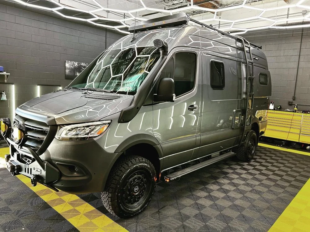 Olive green Mercedes-Benz Sprinter 4x4 camper van with roof rack and all-terrain tires