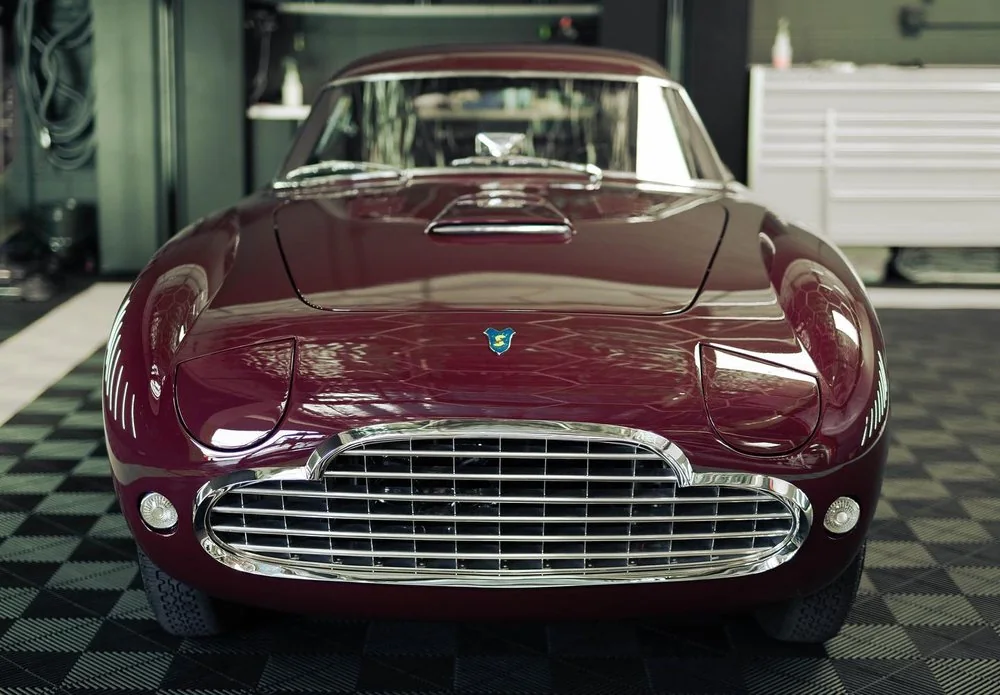 Chrome grille and front end detail of a dark red classic sports car undergoing restoration