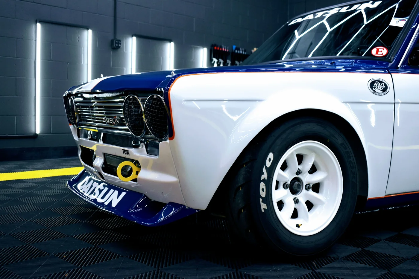 Blue and white Datsun race car with number roundels in the Artec workshop