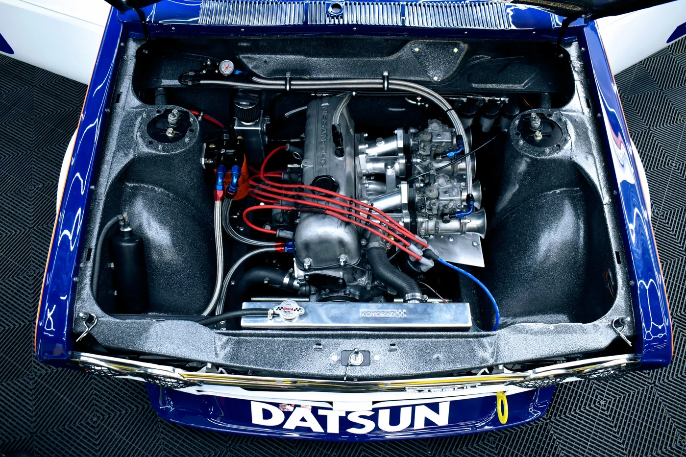 Engine bay of a Datsun race car with custom plumbing and radiator