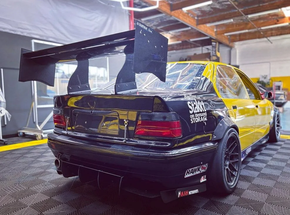 Race car fitted with a large rear wing and aerodynamic bodywork in the fabrication bay