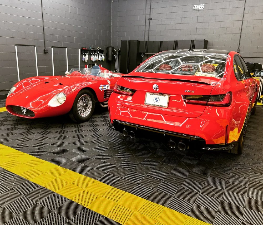 Classic red Ferrari and a red BMW M car parked together inside the Artec Automotive shop