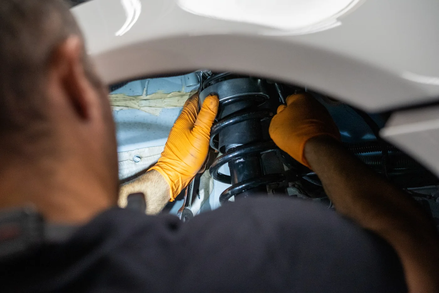 Technician replacing a front coil spring and strut on a white car at Artec Automotive