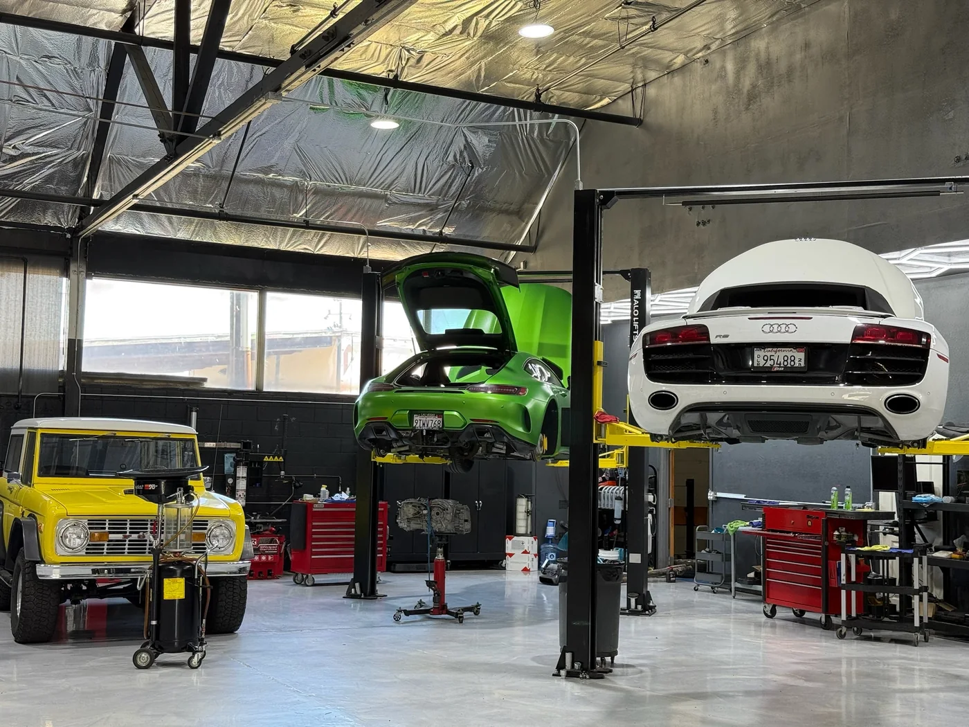 Green Porsche GT3 and a white sports car on lifts in the Artec service bay