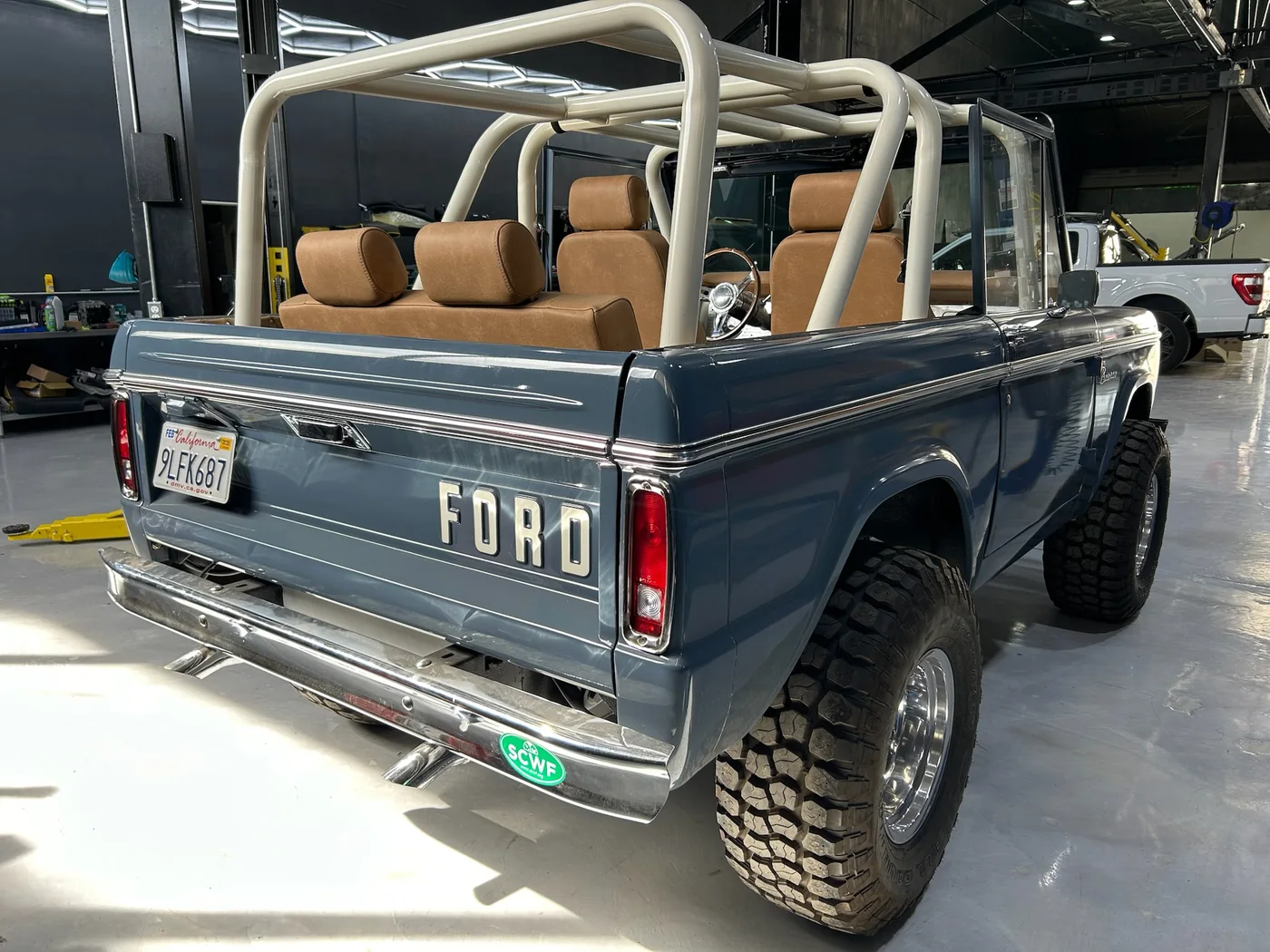 Rear three-quarter view of a restored blue Ford Bronco with roll bar