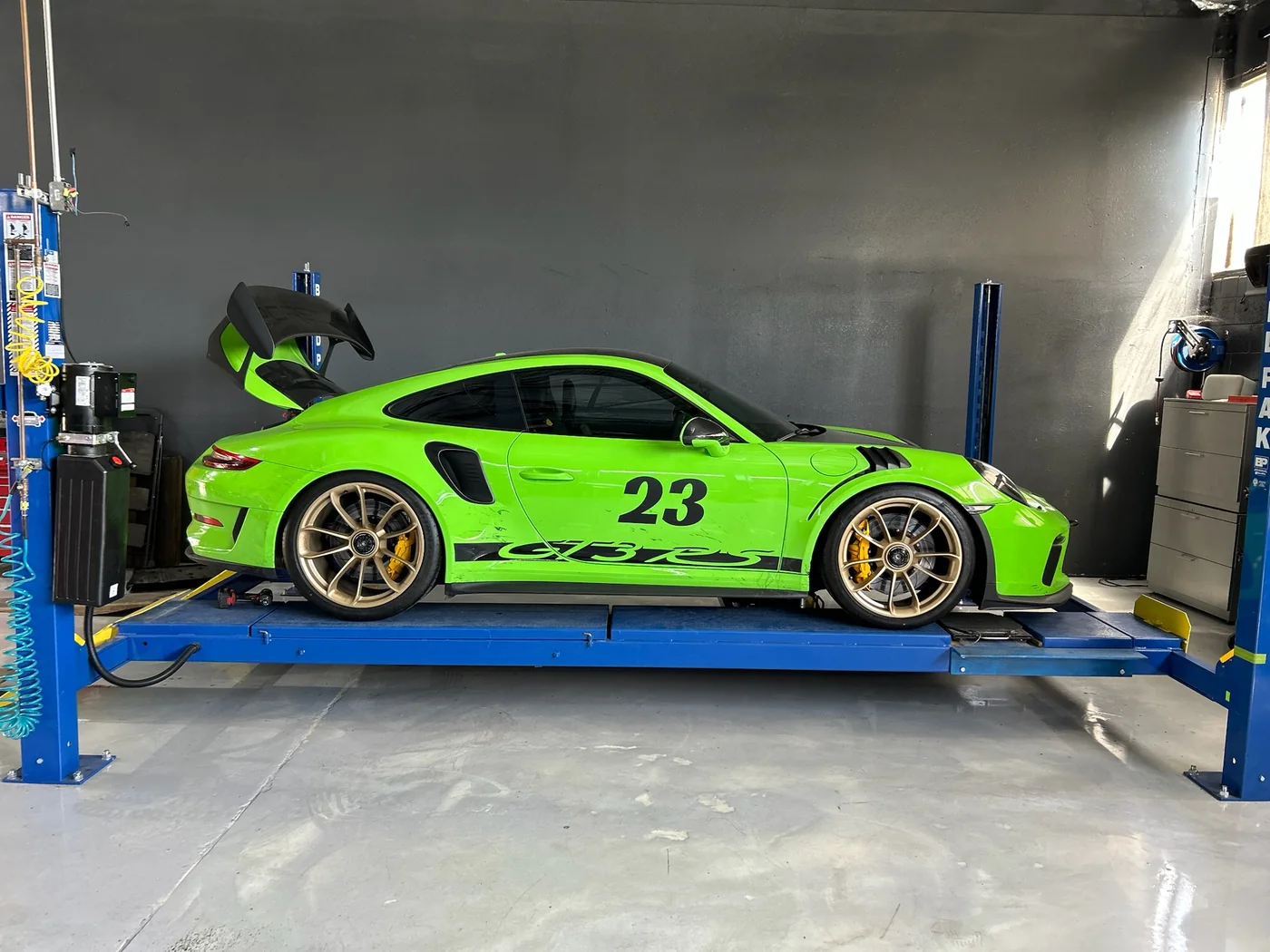 Green Porsche 911 GT3 RS with racing number on a lift at Artec Automotive