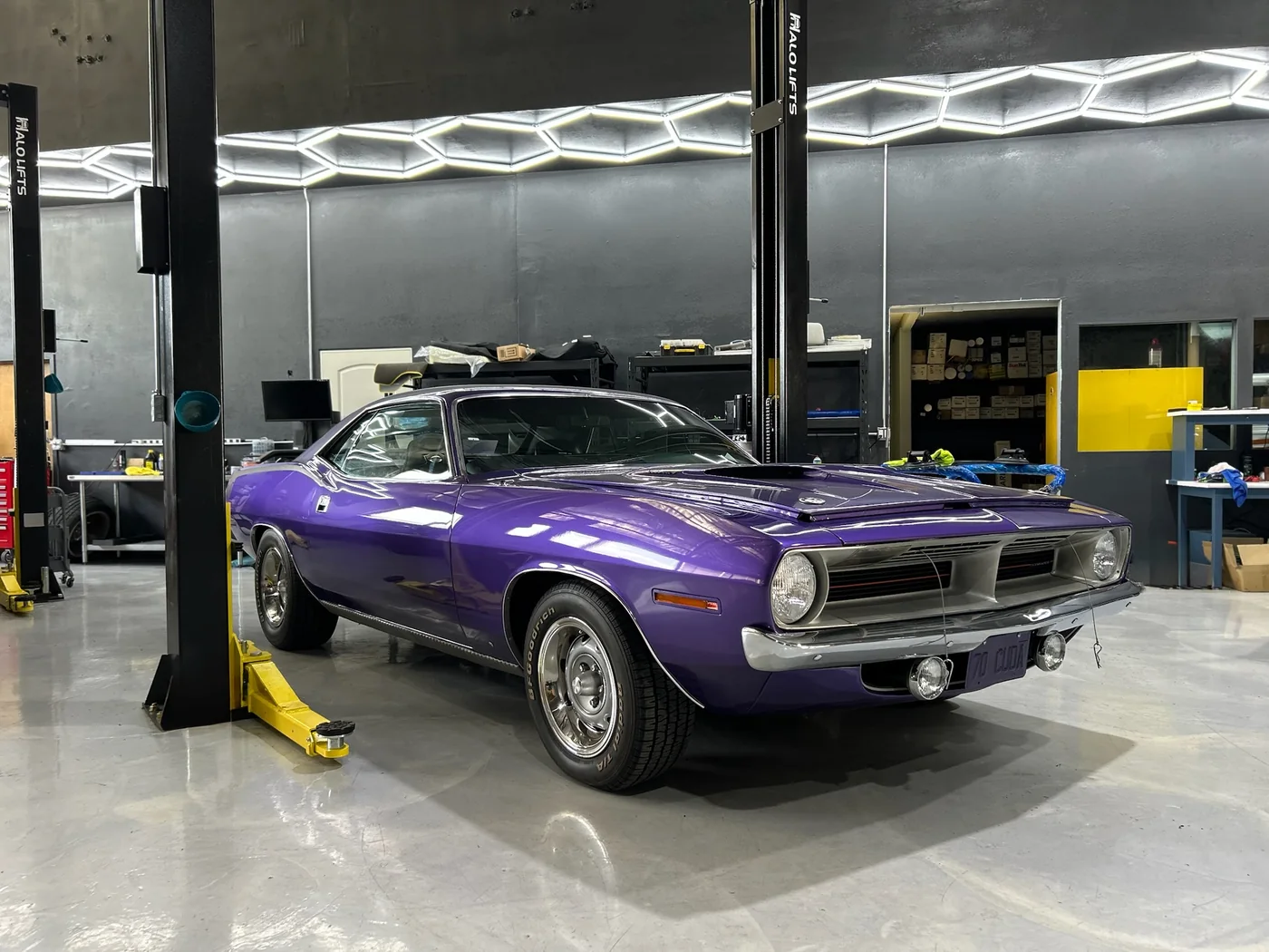 Purple Plymouth Barracuda muscle car raised on a lift in the workshop