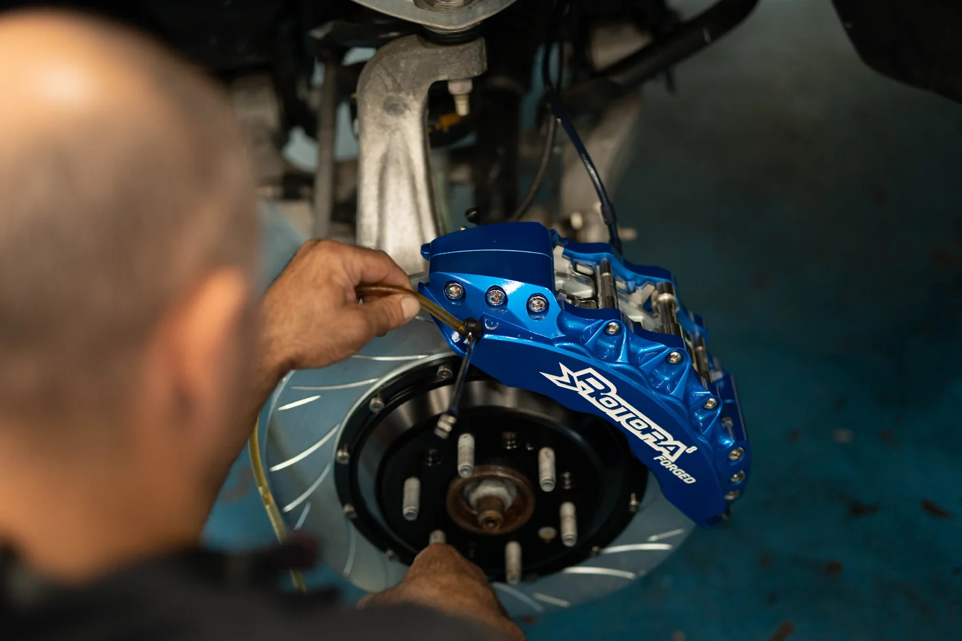Technician bleeding a blue Rotora big brake caliper during a brake upgrade at Artec Automotive